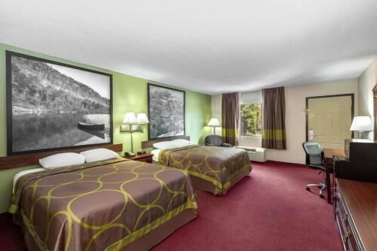 Habitación de hotel con dos camas, un escritorio, una silla y una ventana con cortinas.