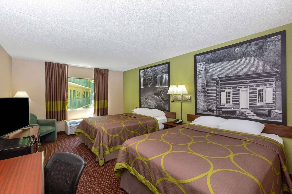 Habitación de hotel con dos camas, un escritorio, un televisor y una ventana con cortinas.