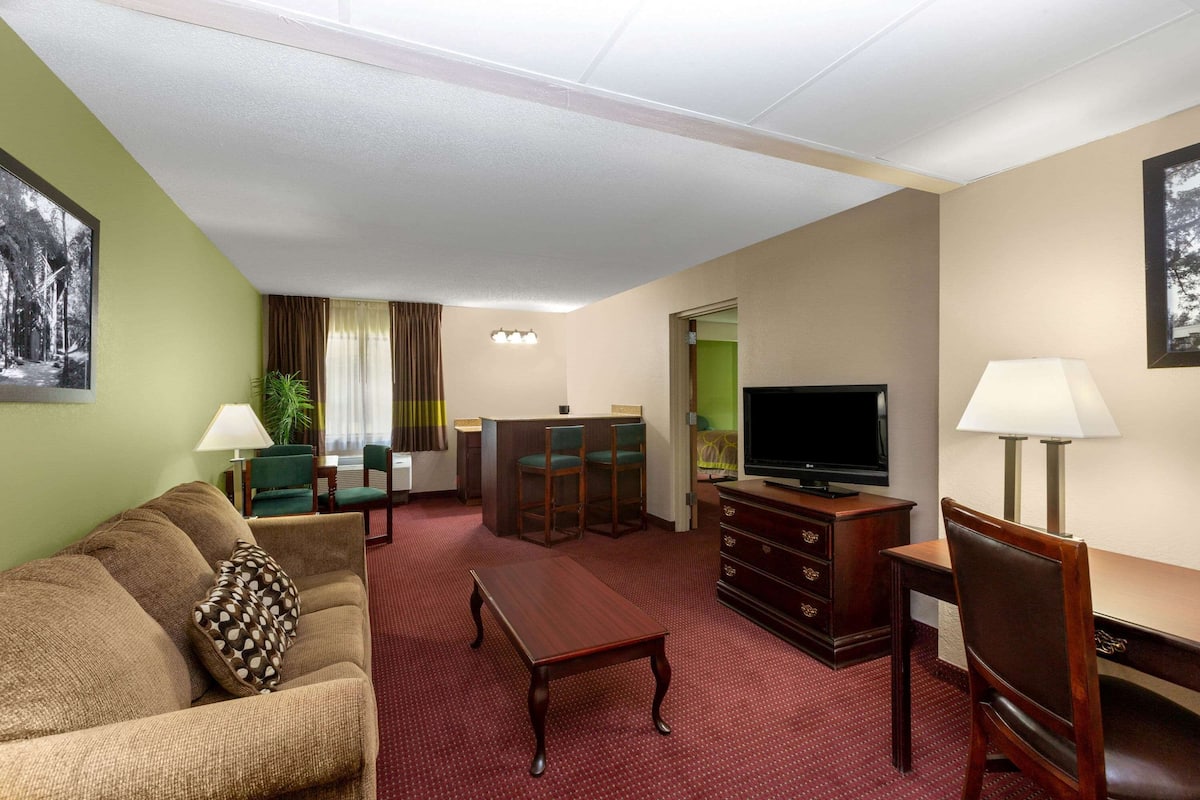 Una habitación de hotel con sofá, mesa de centro de madera, televisión, escritorio y una silla.