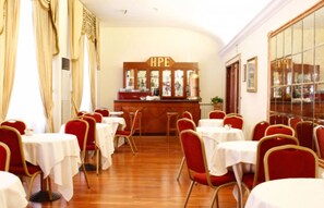 A dining area with round tables and red chairs, a bar with a sign reading "HPE", and a large window with a view of the city. - Pace Helvezia (Rome)
