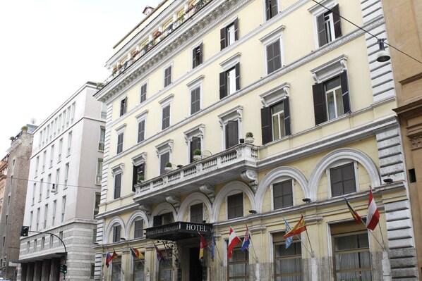 En historisk hotellbyggnad med en klassisk fasad, flera balkonger och ett antal flaggor som vajar utanför.