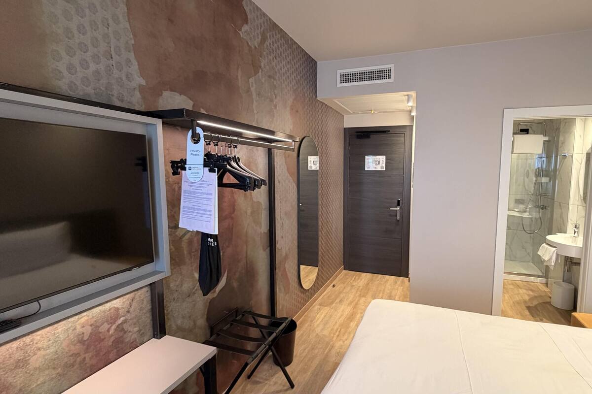 A modern hotel room with a large bed, a TV, a mirror, and a shower area.