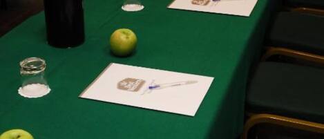 Una mesa de conferencias con manteles verdes, tarjetas de identificación, manzanas, una botella de Coca-Cola y vasos.