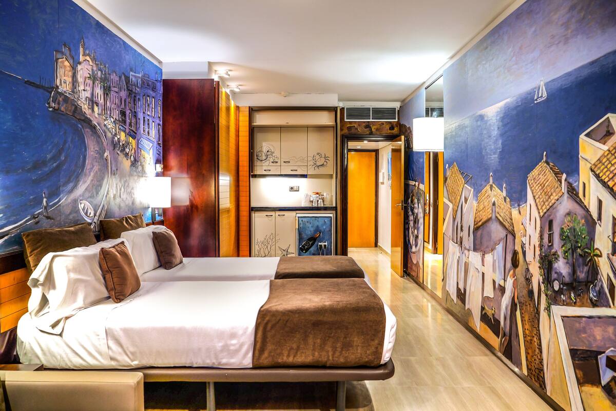 A hotel room with a large bed, a desk, and a mural depicting a coastal scene.
