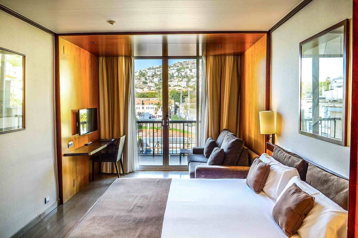 A hotel room with a bed, a desk, a chair, a sofa, and a TV.