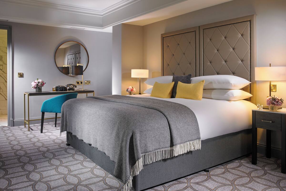 A modern hotel room with a large bed, a desk, a chair, and a round mirror.