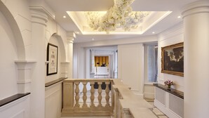 A grand hallway with a marble staircase, a reception desk, and a framed painting on the wall. - The Davenport (Dublin)