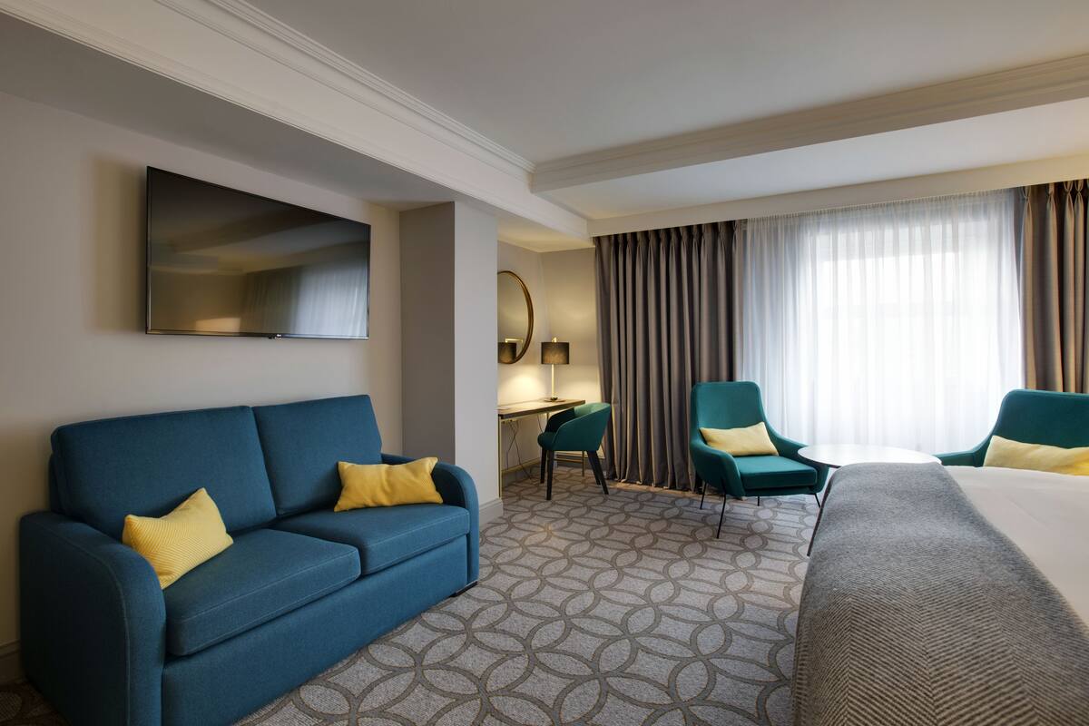 A hotel room with a blue sofa, two armchairs, a bed, a desk, and a TV.