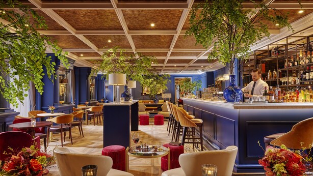 A bar area with a bartender, seating with red ottomans, and a bar counter with various bottles. - The Davenport (Dublin)