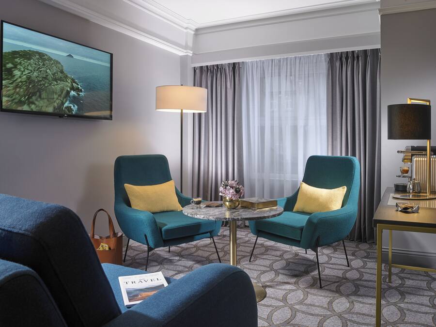Habitación de hotel con dos sillones azul verdosos, una mesa redonda de centro, una lámpara, un televisor y vistas al mar.