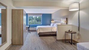 Een hotelkamer met een bed, nachtkastje, lamp en een raam met uitzicht op bomen.