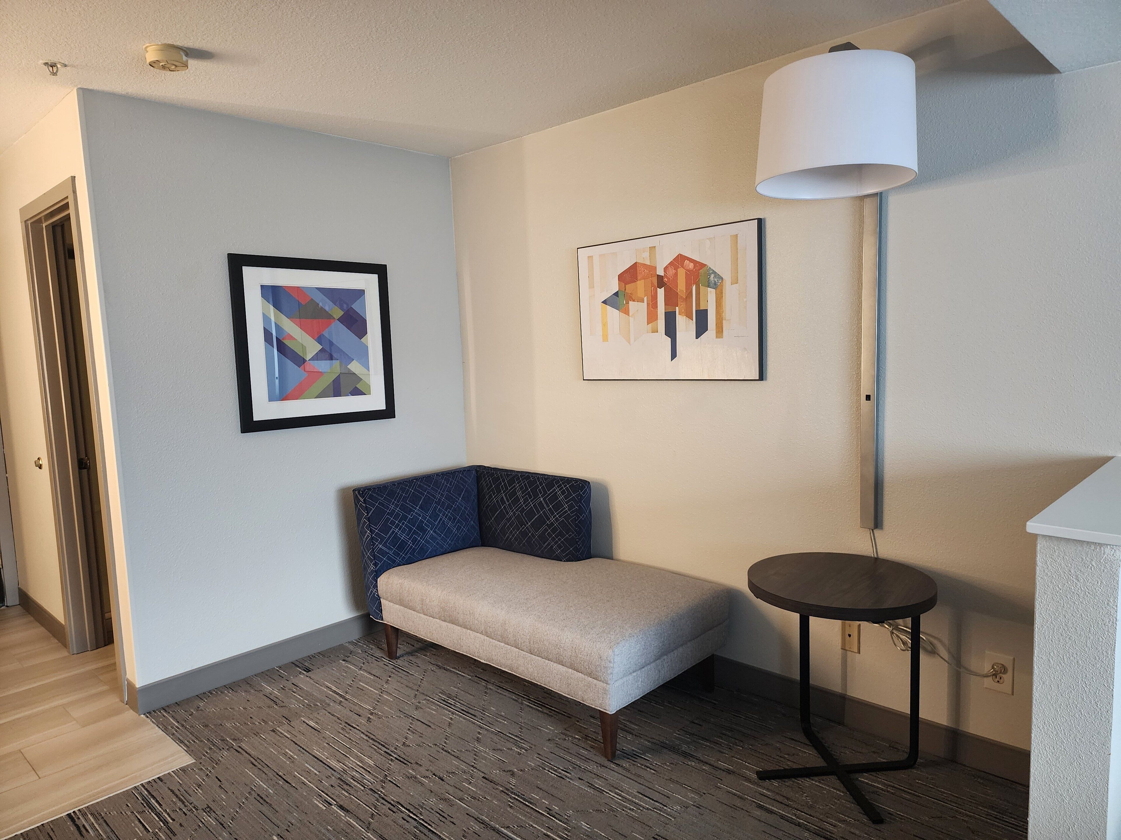 A corner room with a cushioned bench, a small round table, and two framed artworks on the wall.
