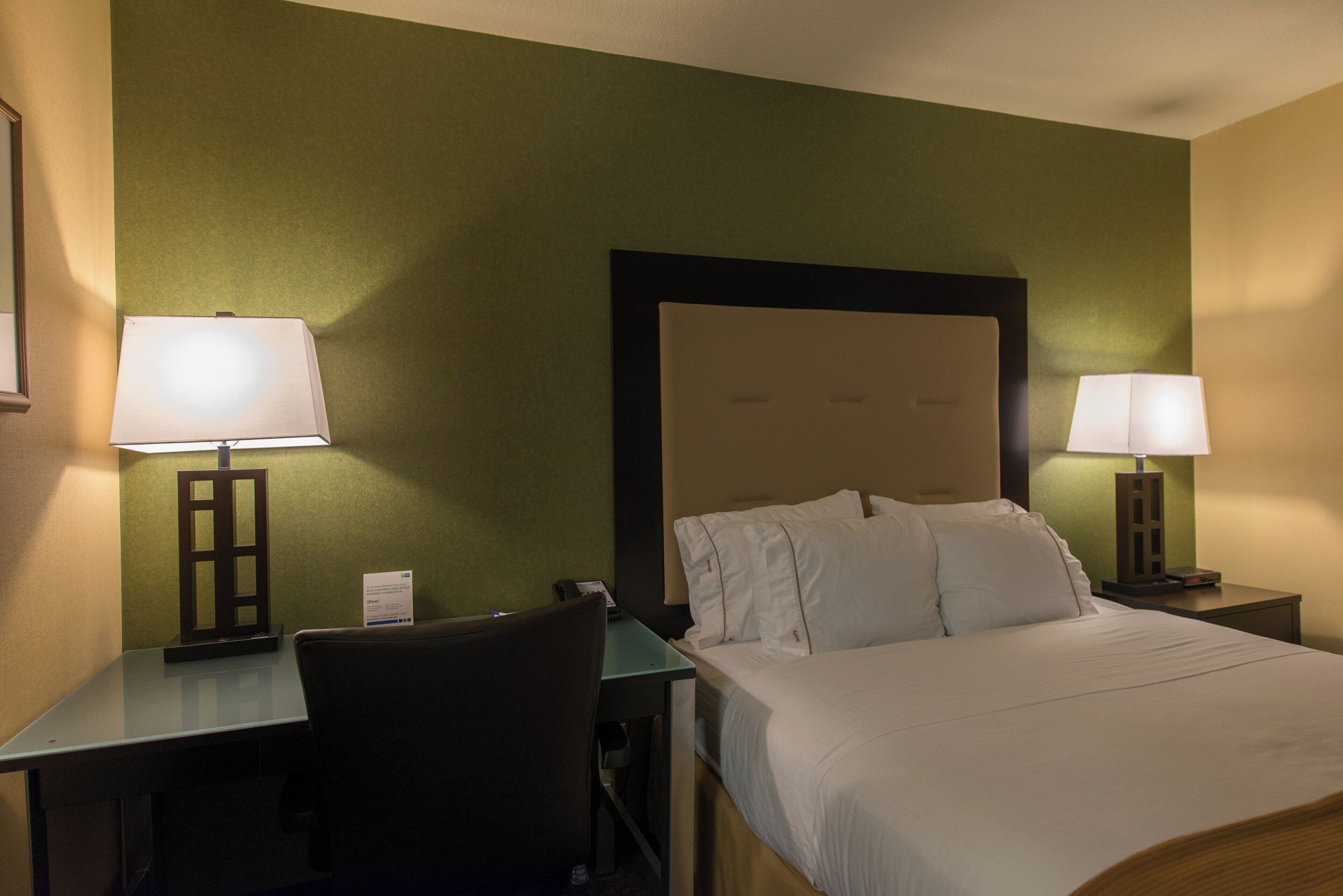A hotel room with a bed, two bedside tables with lamps, a desk, and a chair.