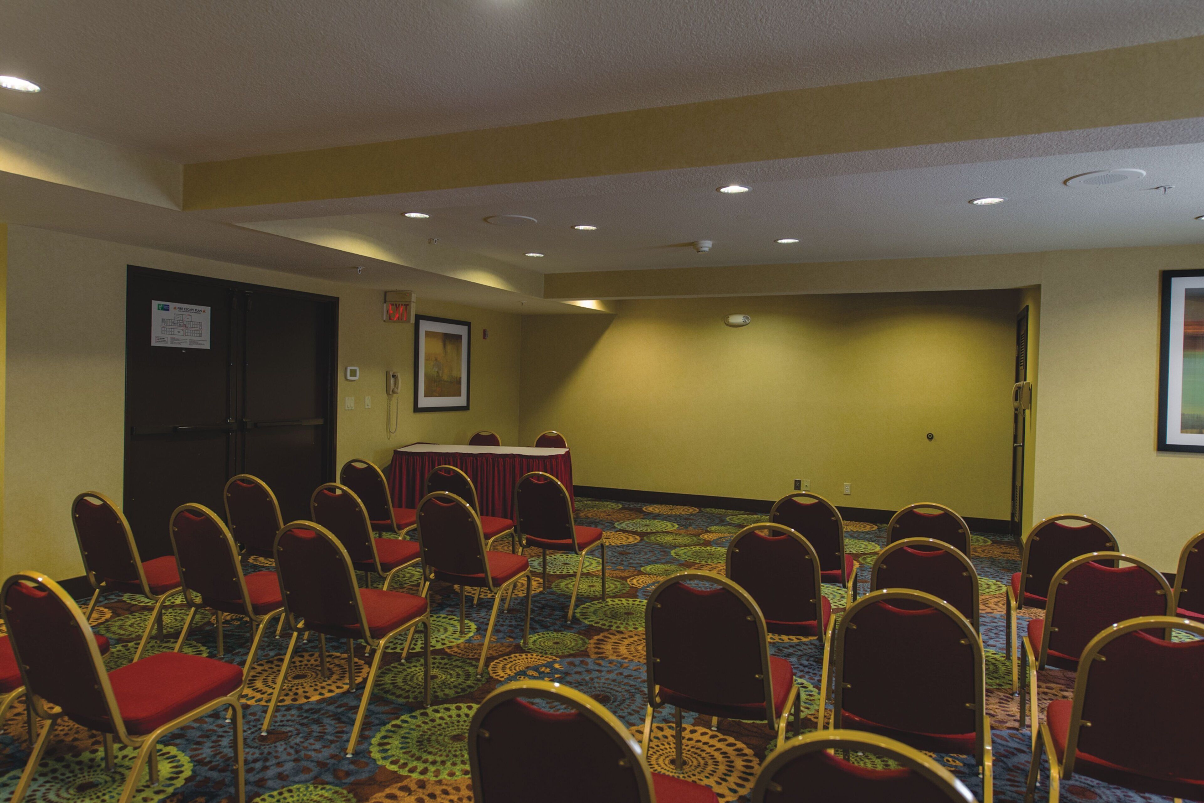 Une salle de conférence avec des rangées de chaises, une table et une porte.