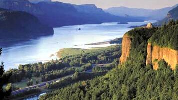 Paisaje montañoso con un río, bosque denso y un acantilado con una estructura en la cima.