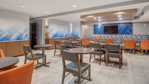 A modern restaurant with round tables and chairs, a TV mounted on the wall, and a patterned backsplash.