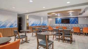 A modern restaurant with round tables and chairs, a TV mounted on the wall, and a patterned backsplash.