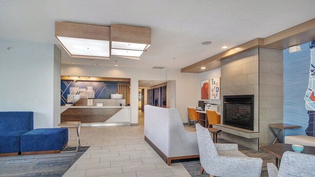 Een moderne hotellobby met een receptiebalie, zithoek en een open haard.