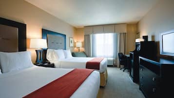 Ein Hotelzimmer mit zwei Betten, einem Schreibtisch, einem Stuhl, einem Fernseher und einem Fenster mit Vorhängen.