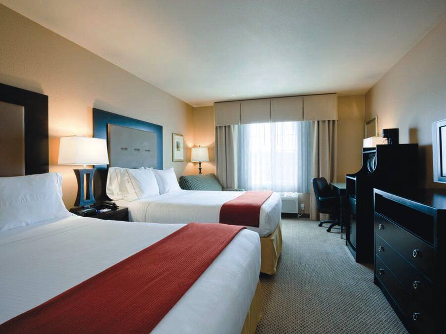 Ein Hotelzimmer mit zwei Betten, einem Schreibtisch, einem Stuhl, einem Fernseher und einem Fenster mit Vorhängen.