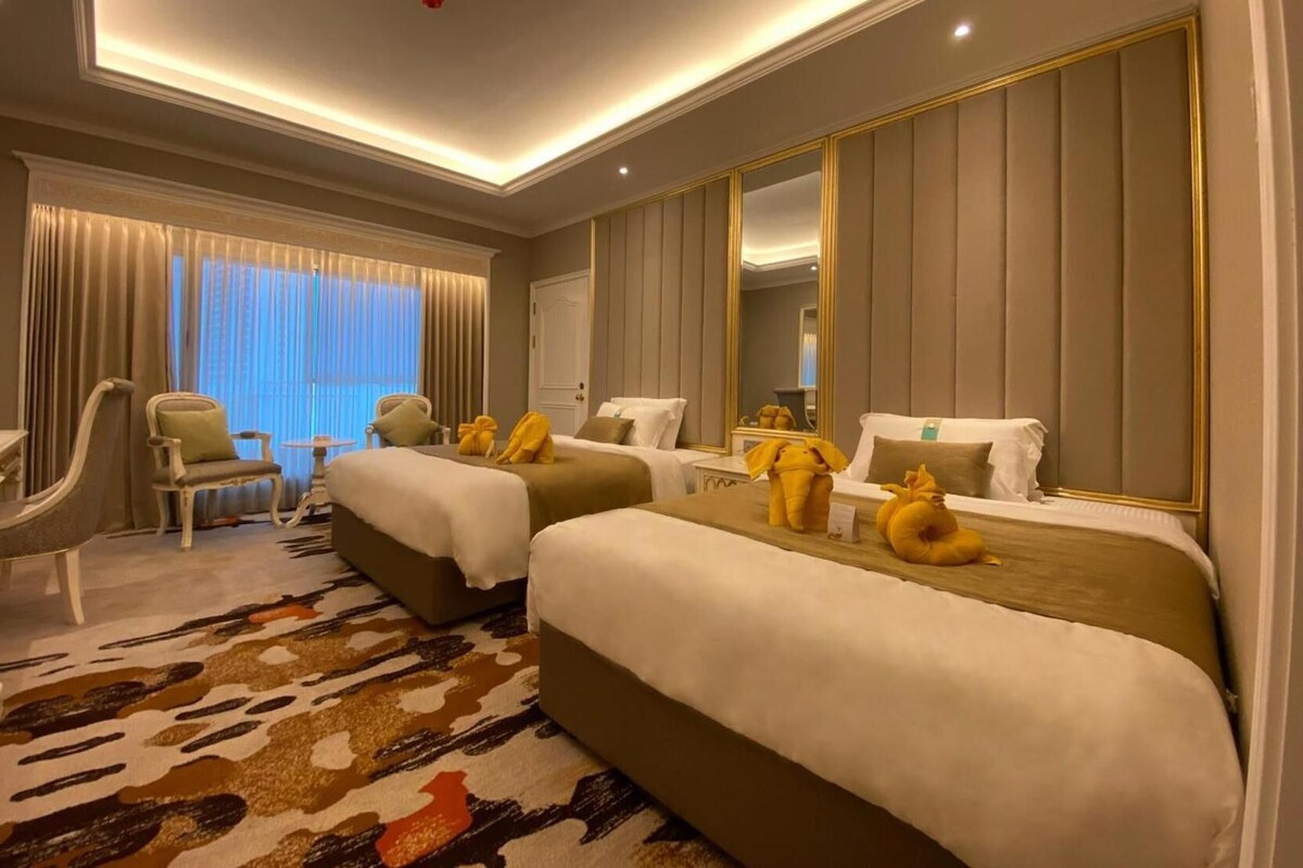 A hotel room with two beds, a large mirror, a chair, and a patterned carpet.