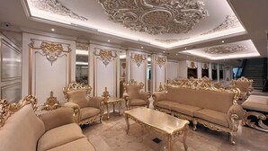A luxurious room with ornate gold detailing, plush seating, and a grand ceiling design.
