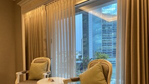 A room with two ornate chairs, a small round table, and a view of a cityscape through sheer curtains.