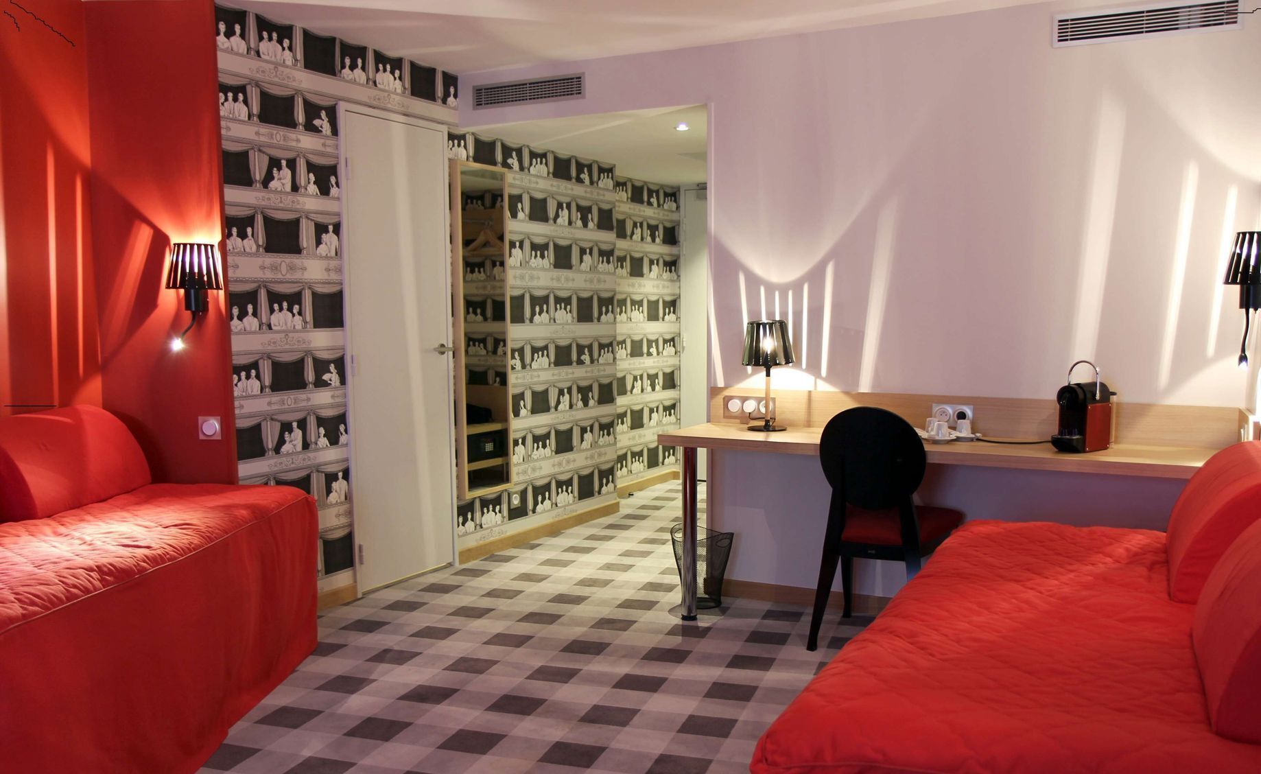 A hotel room with a checkered floor, a desk with a chair, and two red beds.
