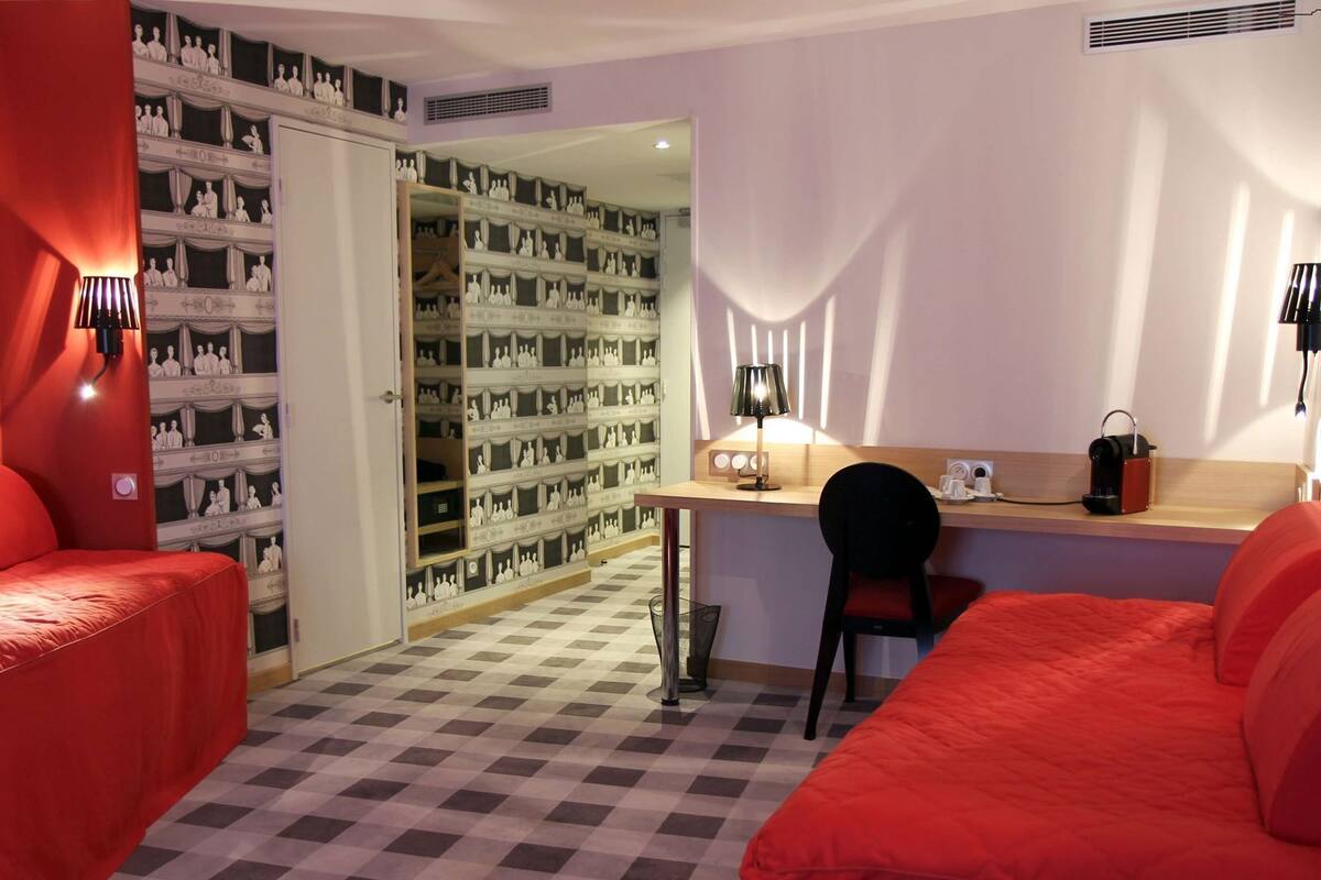 A hotel room with a checkered floor, a desk with a chair, and two red beds.