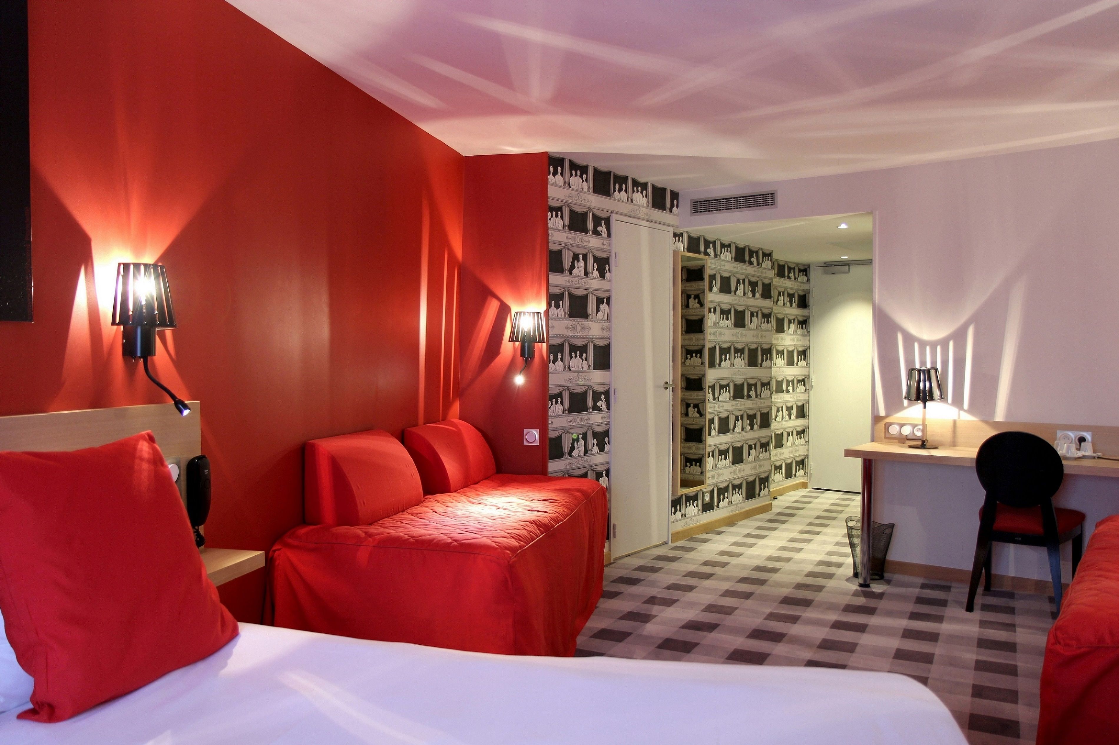 A hotel room with a red and white color scheme, a bed, a desk, and a chair.