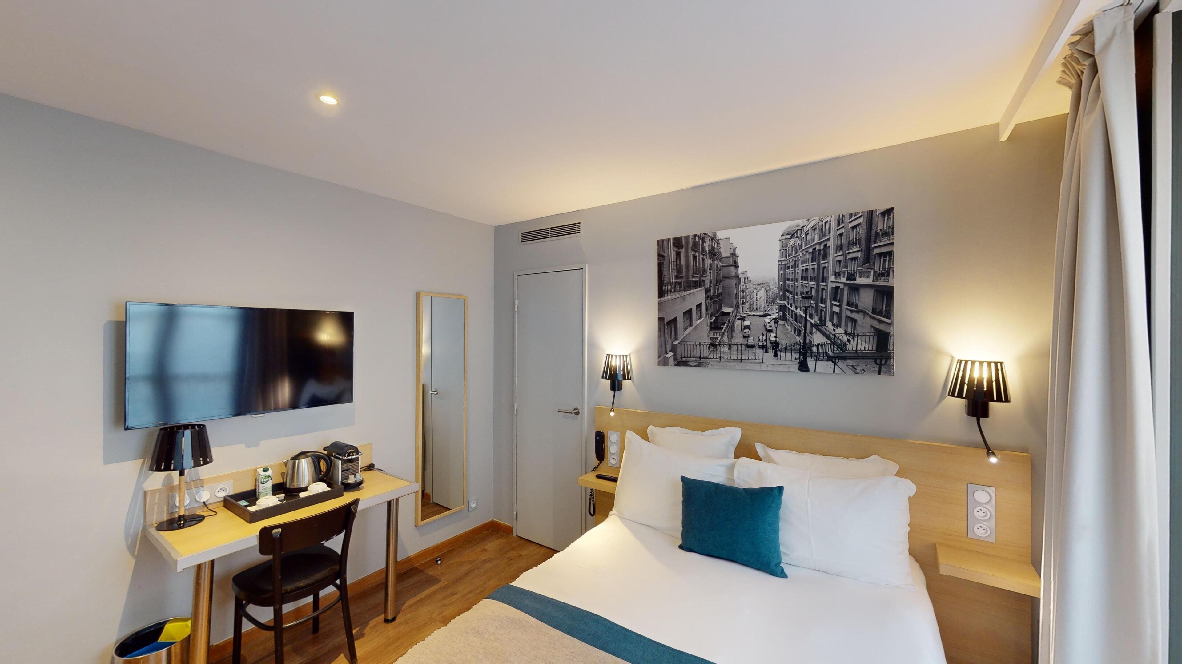 A hotel room with a bed, a desk, a television, a painting, and a lamp.