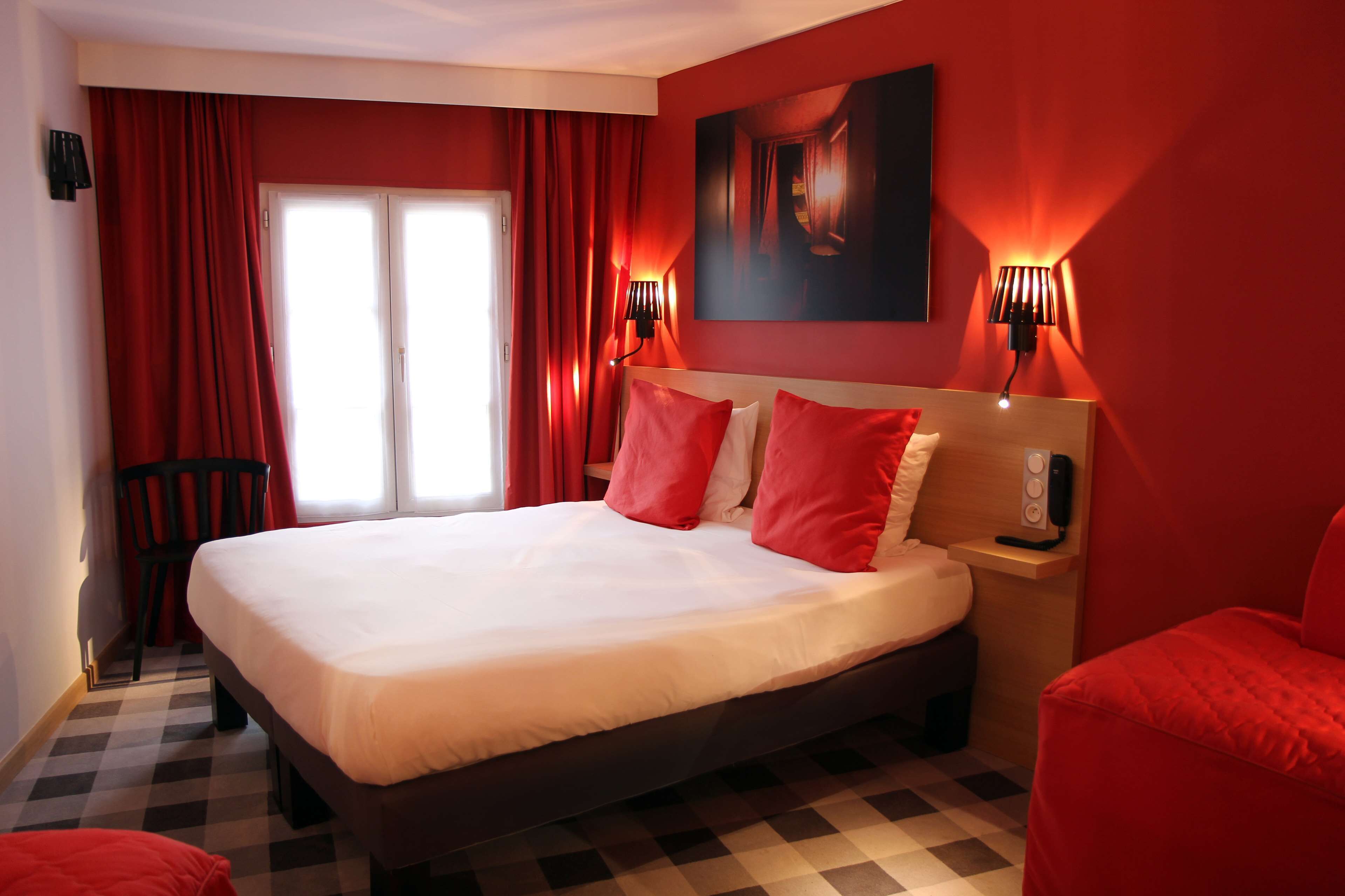 A hotel room with a large bed, red curtains, a checkered floor, and a painting on the wall.