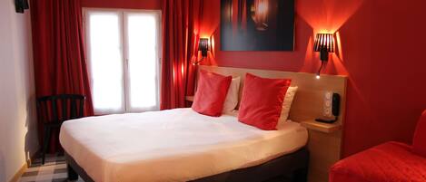 A hotel room with a large bed, red curtains, a checkered floor, and a painting on the wall.
