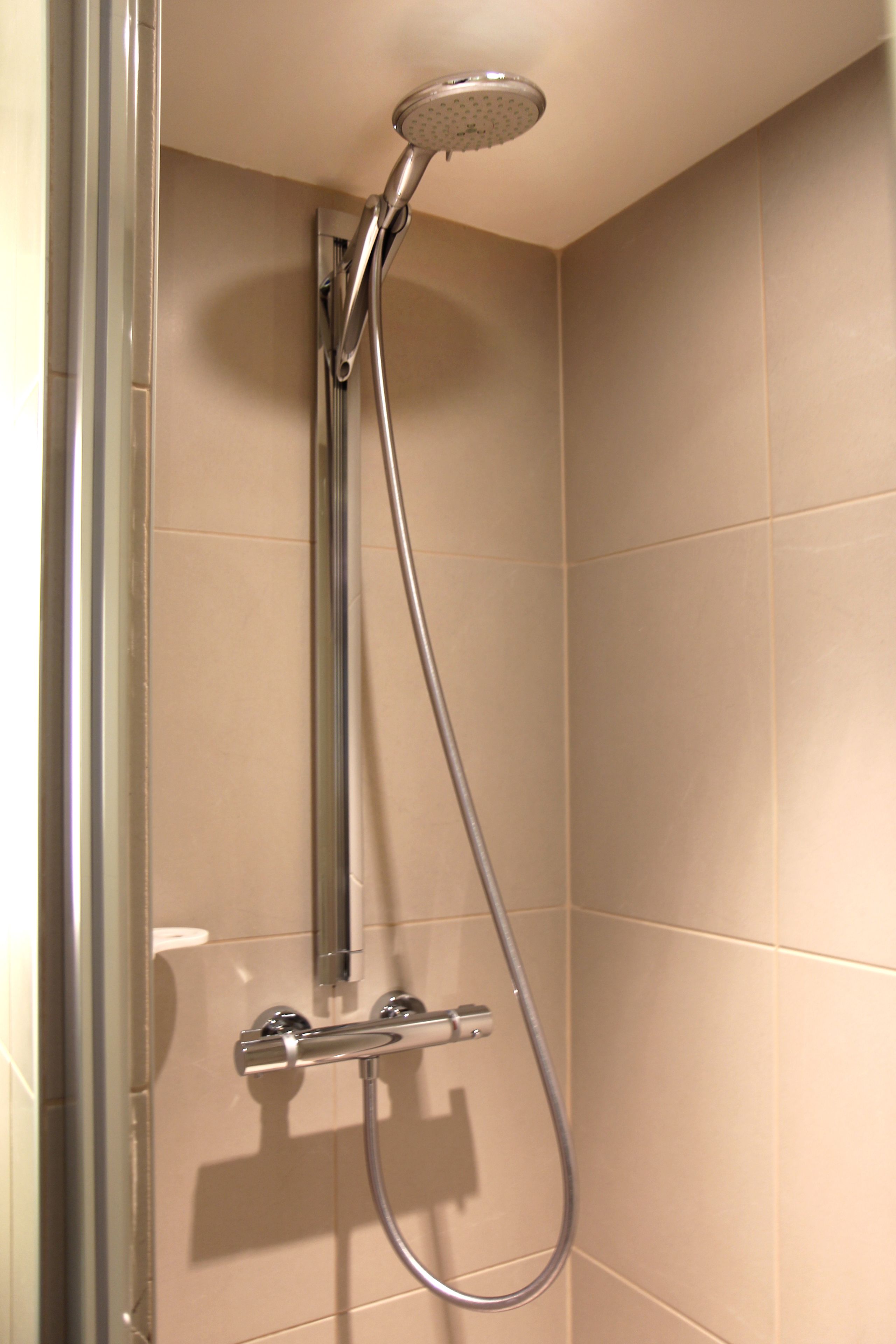 A shower with a handheld showerhead and a wall-mounted control panel.