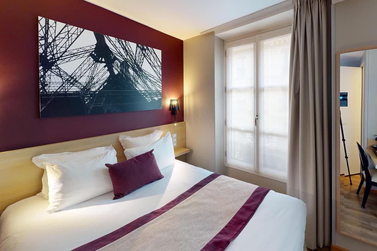 A hotel room with a large bed, a desk, and a chair.