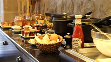 Montaje de bufé con diferentes alimentos, una cesta de huevos, una botella de kétchup Heinz y una olla negra sobre la encimera.