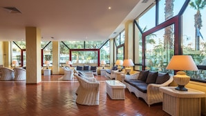 A spacious lobby with wicker furniture, large windows, and a tiled floor. - Dom Pedro Marina (Loulé)