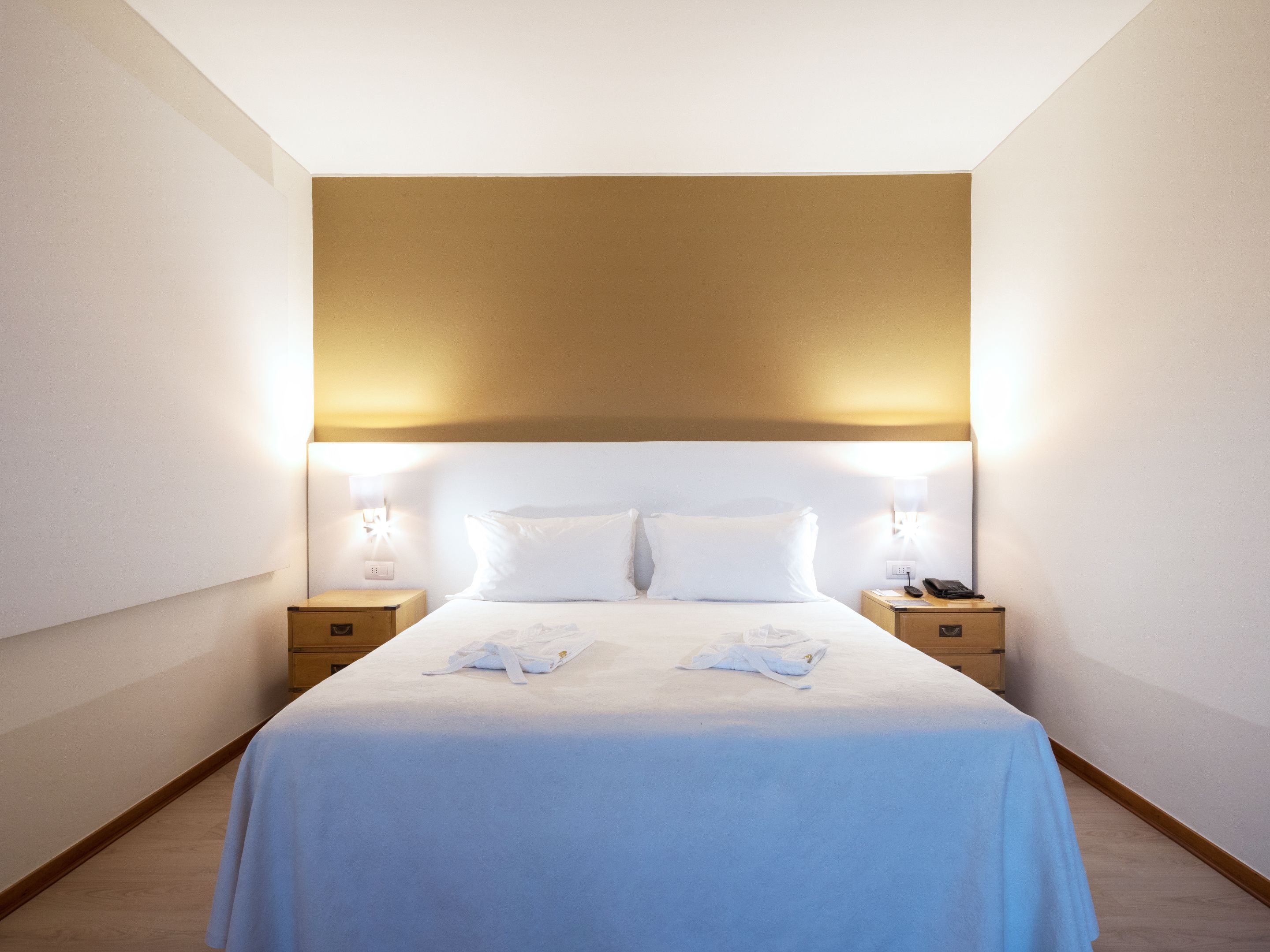 A hotel room with a large bed, two bedside tables, and a headboard with integrated lighting.