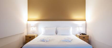 A hotel room with a large bed, two bedside tables, and a headboard with integrated lighting.
