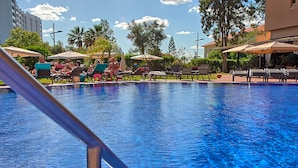 A swimming pool with lounge chairs and umbrellas, surrounded by greenery and buildings. - Dom Pedro Marina (Loulé)