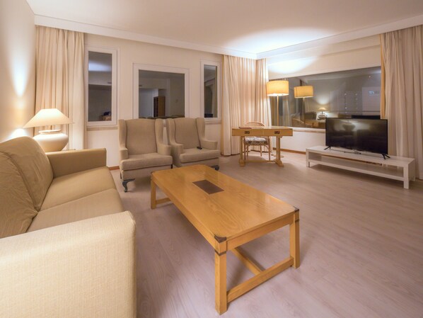 Una sala moderna con un sofá, dos sillones, una mesa de centro de madera, un televisor sobre un mueble bajo y una mesa de comedor con sillas.
