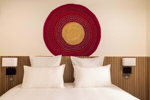 Habitación de hotel con una cama, dos lámparas de noche y un adorno circular en la pared.