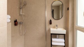 A modern bathroom with a shower, a sink, and a mirror. - Korner Louvre (Paris)