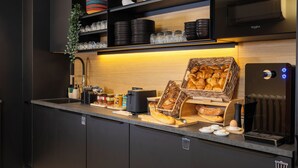 A modern kitchen with black cabinets, a built-in oven, and a coffee machine. - Korner Louvre (Paris)