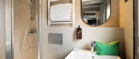 A modern bathroom with a glass-enclosed shower, a white sink, a mirror, and a towel rack.