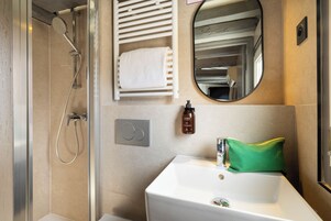 A modern bathroom with a glass-enclosed shower, a white sink, a mirror, and a towel rack.