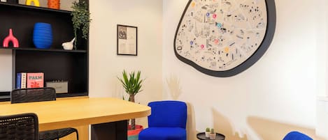 A modern room with a wooden table, blue chairs, a black bookshelf, and a large wall map.