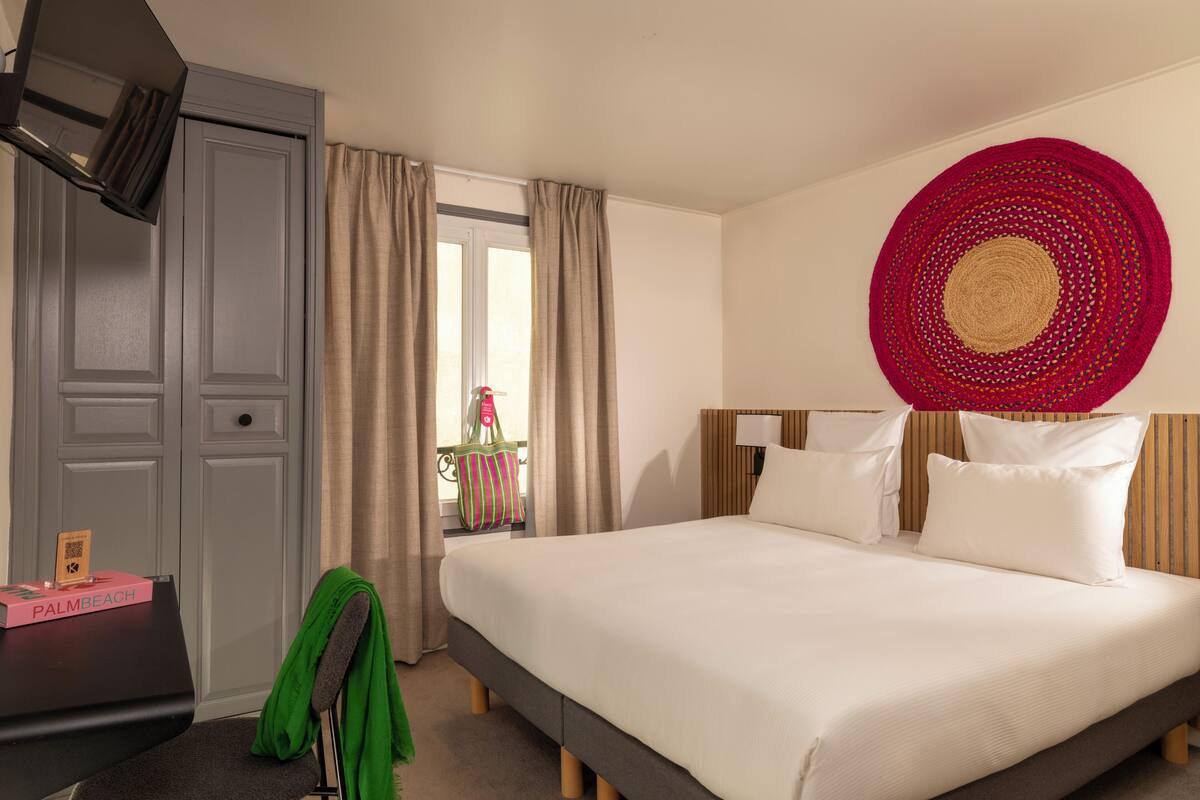 Hotelkamer met een bed, bureau, stoel, groene handdoek en een ronde rode decoratie aan de muur.