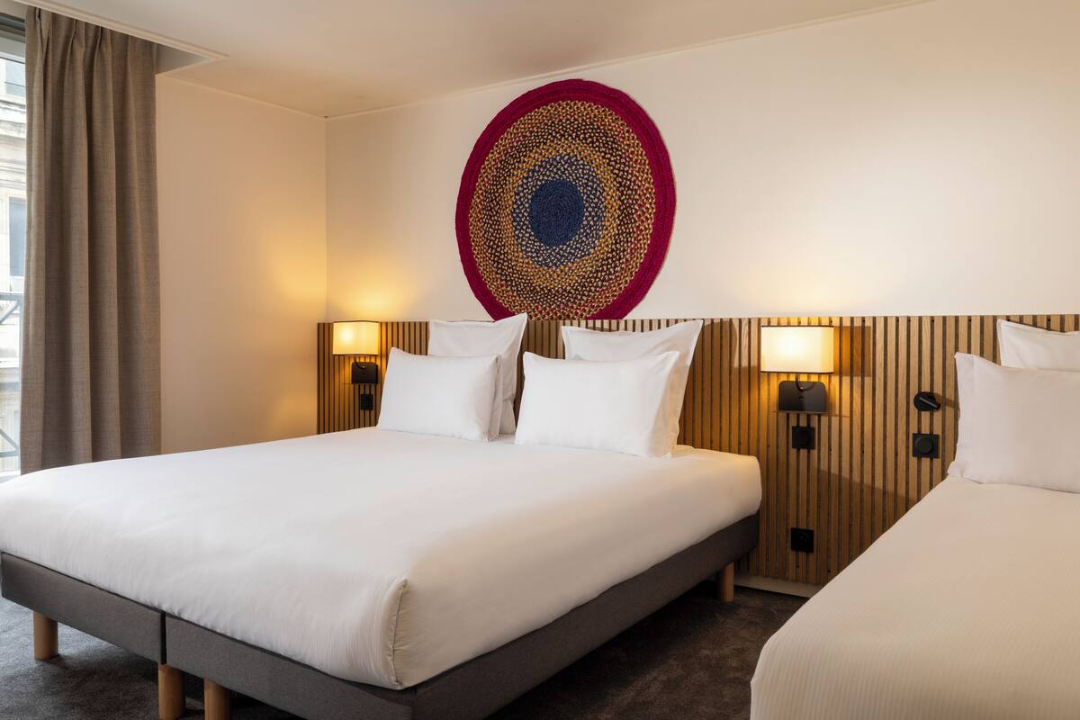 Een hotelkamer met een groot bed, twee nachtkastjes met lampen, een houten hoofdeinde en een decoratieve wanddecoratie.