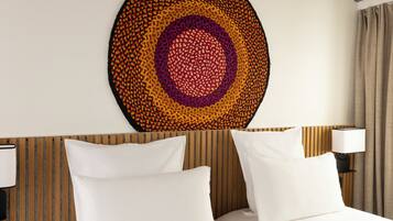 Une chambre d’hôtel avec un lit, des oreillers blancs, une œuvre d’art murale de forme circulaire et une tête de lit en bois.